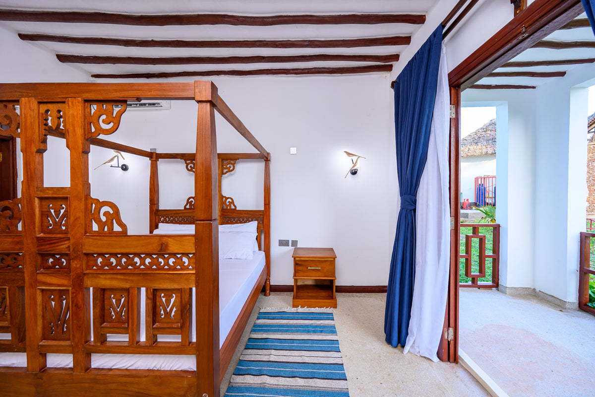 Carved four-poster bed with mosquito net in the Family Cottage bedroom at Kasa Pomboo